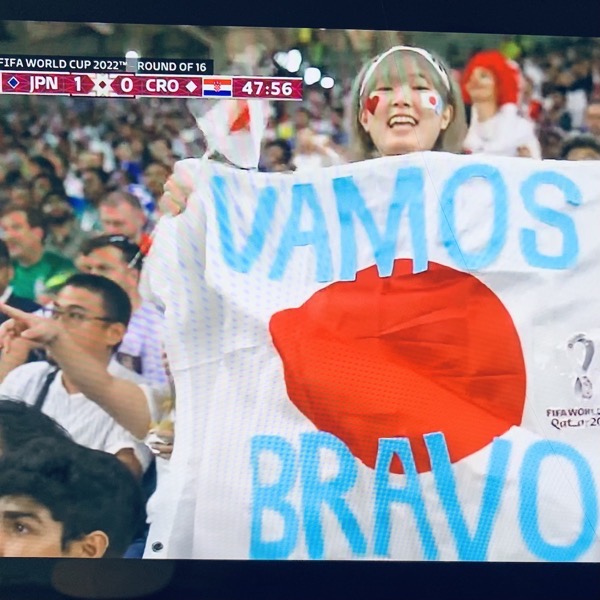a fan at the Japan vs. Croatia World Cup game holds a Japanese flag with the Spanish words 'Vamos' and 'Bravo'